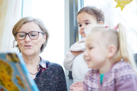 Eine Erzieherin liest zwei kleinen Mädchen ein Bilderbuch vor.