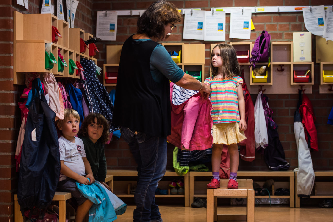 Eine Erzieherin hilft einem Mädchen beim Anziehen der Jacke.