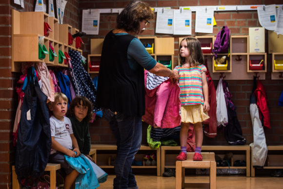 Eine Erzieherin hilft einem Mädchen beim Anziehen der Jacke.