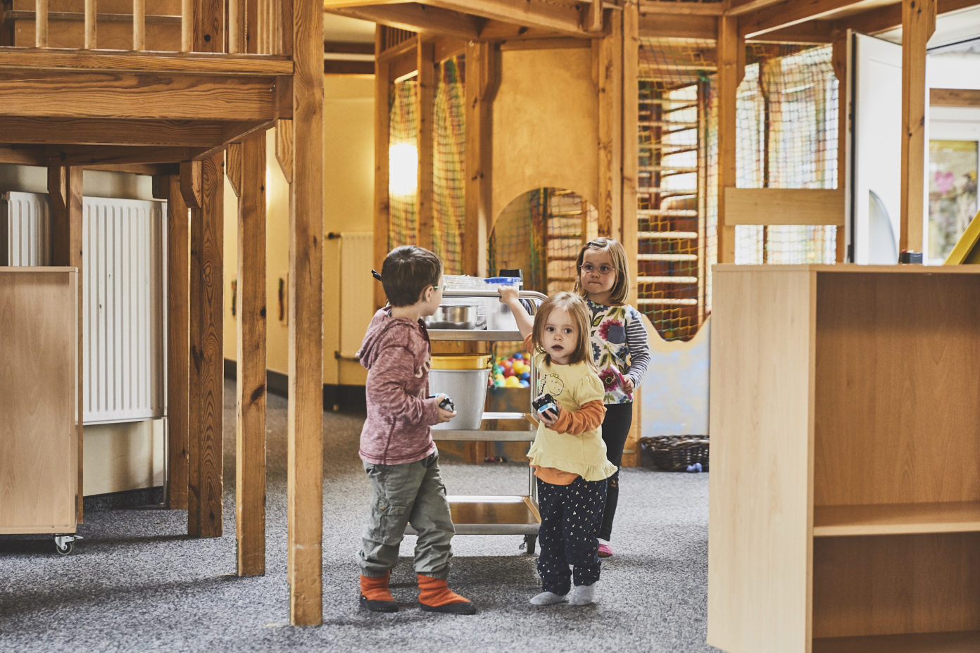 Drei Kinder schieben einen Frühstückswagen durch die Kita.