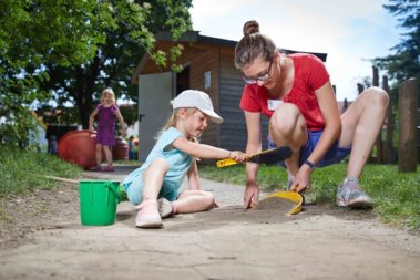 Ein kleines Mädchen hilft ihrer Erzieherin beim Fegen eines Gartenweges der Kita.
