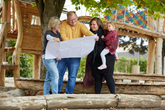 Eltern mit einem Bauplan in der Hand vor einem Klettergarten.