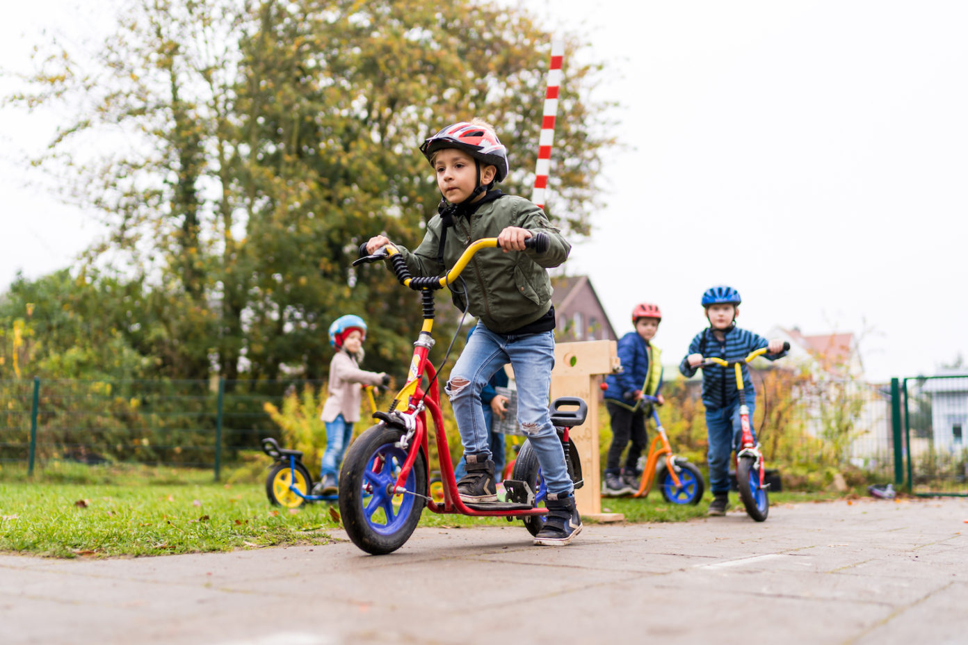 Drei Jungs und ein Mädchen fahren auf dem Weg vor ihren Häusern mit ihren Rollern.