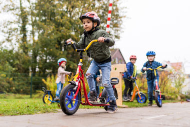 Drei Jungs und ein Mädchen fahren auf dem Weg vor ihren Häusern mit ihren Rollern.