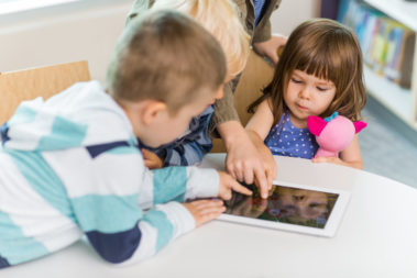 Cute girl with friends using digital tablet at table in school library