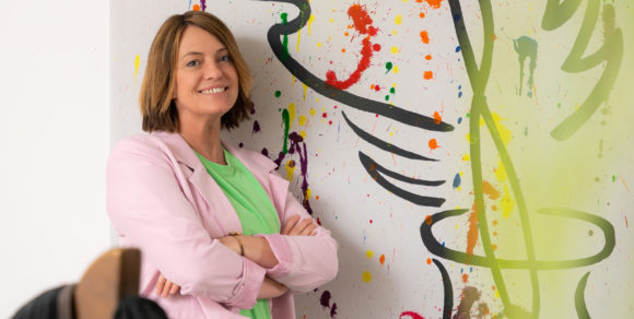 Frau lehnt an bunt bemalter Wand.