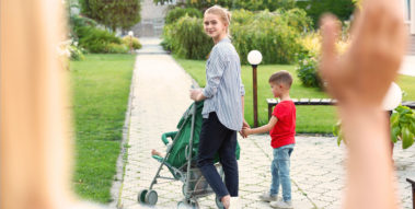 Junge Frau schiebt einen Buggy und hat ein Kind an der Hand