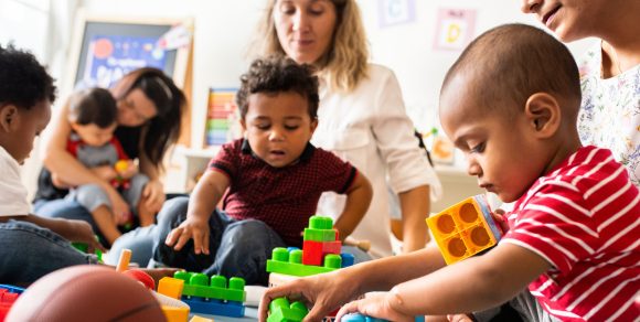 Kinder und Erzieherinnen spielen mit Bauklötzen