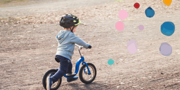Kleiner Junge mit Helm fährt Laufrad.