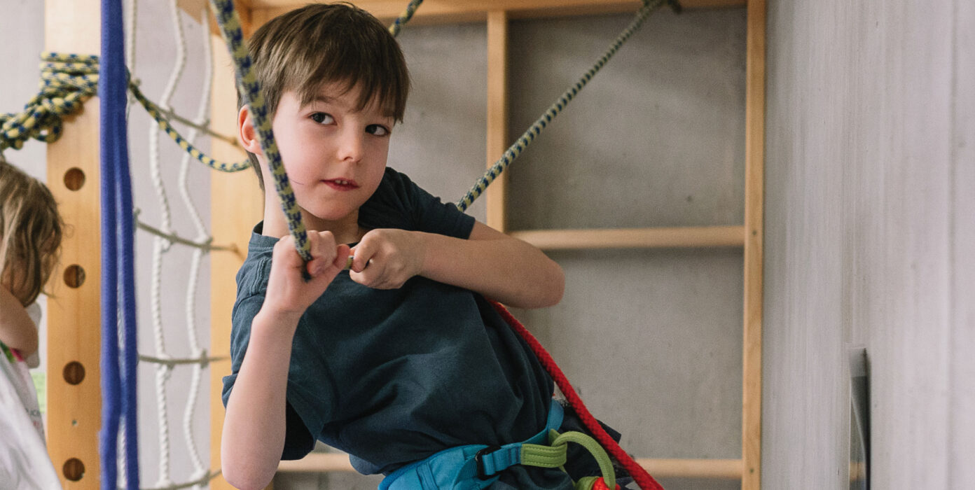 Karl klettert gesichert mit einem Klettergurt durch die Kletterlandschaft im Bewegungsraum.